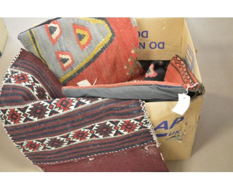 A box of textiles, to include: cushion covers and a woven saddle bag on dark red ground.