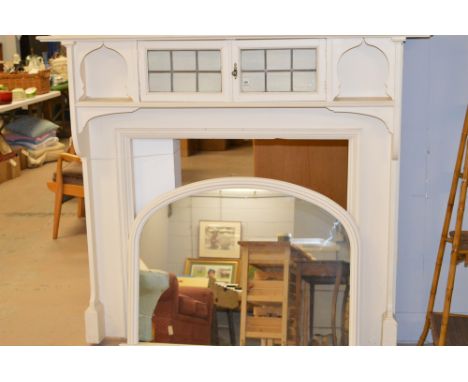 An early 20th Century cream painted fire surround with leaded glass cupboard, 162cms wide; together with a matching arch topp