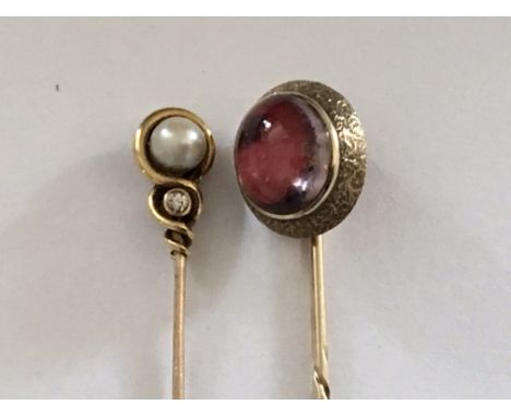 A gold stick pin inset with a garnet cabochon and one other stick pin set with a pearl and diamond. (2)