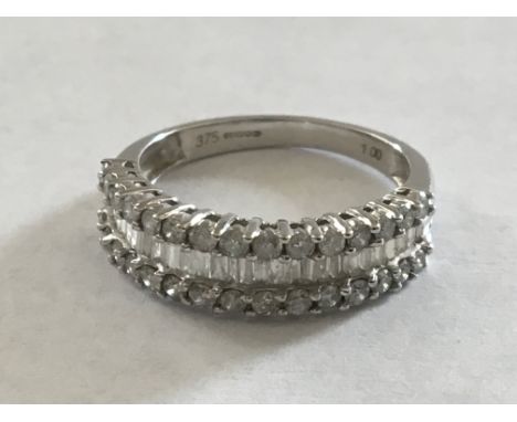 A 9 carat white gold ring set with a row of baguette diamonds flanked by round brilliant cut diamonds. Ring size M.