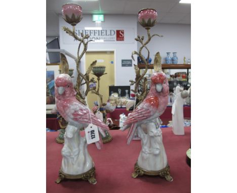 A Pair of Ceramic and Gilt Metal Candlesticks, each as an exotic bird on perch, in pink and white on circular three footed ba