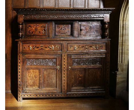 An inlaid oak buffet.17th century and later, the top section with egg and dart and arcaded moulding, a panel carved with scro