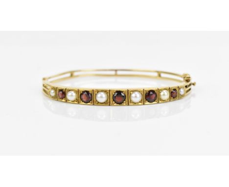 A 9ct yellow gold, pearl and garnet set bangle, set with graduated alternating pearl and red garnet stones, the hinged bracel