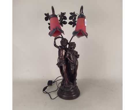 A 20th Century patinated composition two branch table lamp of lovers with two red glass Art Nouveau lamp shades