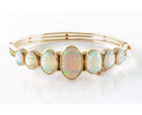AN OPAL HINGED BANGLESet with seven graduated opals, in a rub over setting, on a hinged bangle with tongue and clip clasp, sa