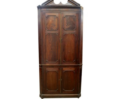 A George III mahogany standing corner cupboard, with dentil moulded broken arch pediment, two double panelled doors with appl