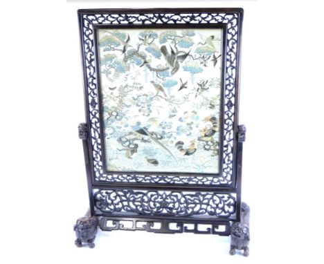A 19thC Chinese hardwood fire screen, centred by a silk work set with flowers and birds in colours, the cared surround on sha