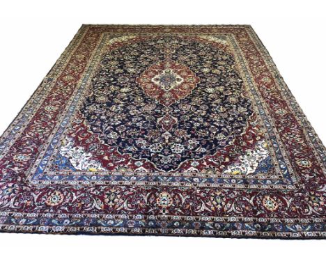 FINE PERSIAN KASHAN CARPET, 395cm x 292cm, central medallion on a palmette and vine midnight blue field within corresponding 