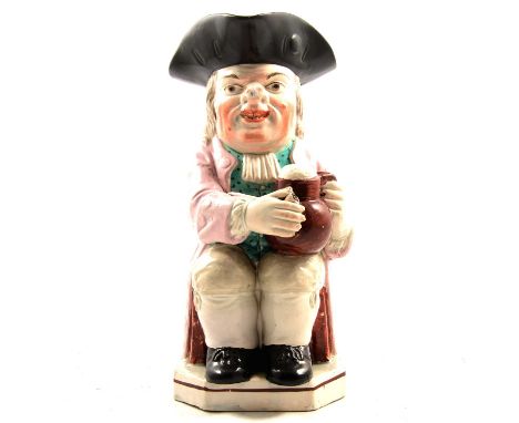 Early 19th century pearlware Toby jug, seated holding a foaming ale jug and smoker's pipe, painted with pale pink overcoat, g