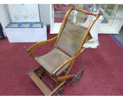 A beech framed Edwardian child's pushchair with worn tapestry back and seat and raised on wheels