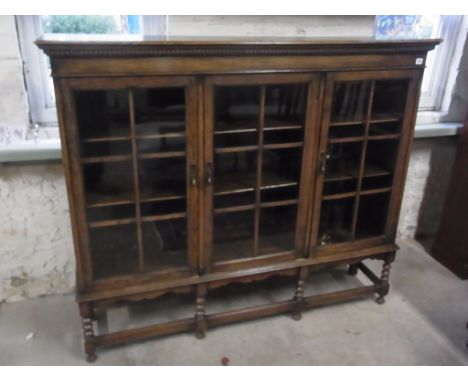 An oak three door glazed bookcase on bobbin supports - Height 130cm x 154cm x 35cm