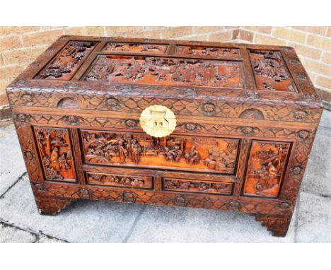 A CAMPHOR WOOD TRUNK, with carved decoration depicting figures amongst foliage with brass clasp to the front a raised on brac