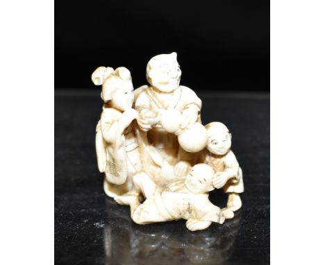 A JAPANESE MEIJI PERIOD CARVED IVORY NETSUKE well modelled as a group of figures including Oni standing, pouring from a doubl