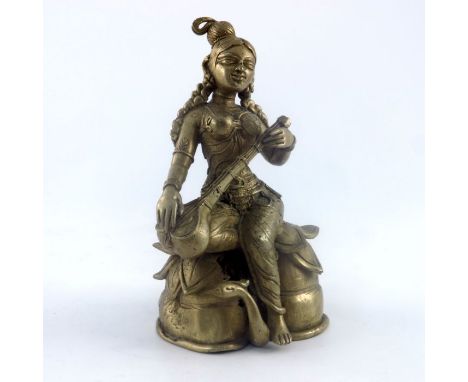 An Indian cast brass figure of a female deity, seated on a lotus leaf playing a string instrument with bird below, height 18c