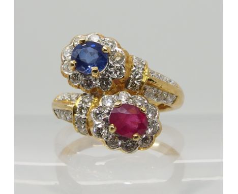 A bright yellow metal dress ring set with diamonds a ruby and a sapphire of twin cross over flower design. Diamond content es