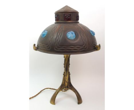 A continental gilded metal table lamp the shade with opalescent and ruby glass nuggets within wavy borders, resting on mistle