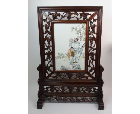 A Chinese polychrome tile screen painted with a ritual figure with water and another pouring into a bowl, within a carved woo