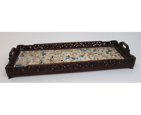 A Chinese hardwood tea tray carved with foliate gallery and scroll handles inset with a pair of silk sleeve panels, 55 x 20cm