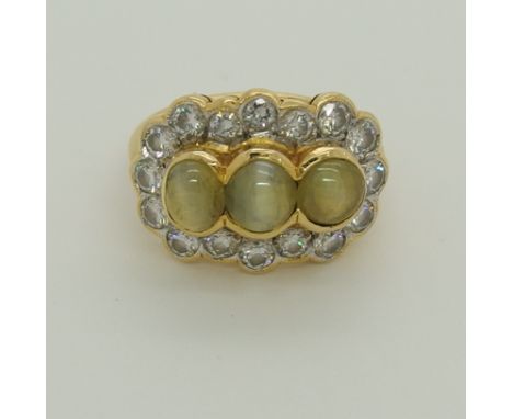 A bright yellow metal ring set with three cats eye chrysoberyls and diamonds to a tapered shouldered shank. Diamond content e