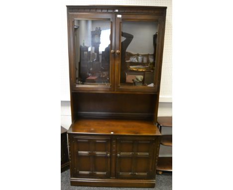 A dark oak Ercol display cabinet , two cross banded glazed doors enclosing shelves, projecting base, above two panelled doors