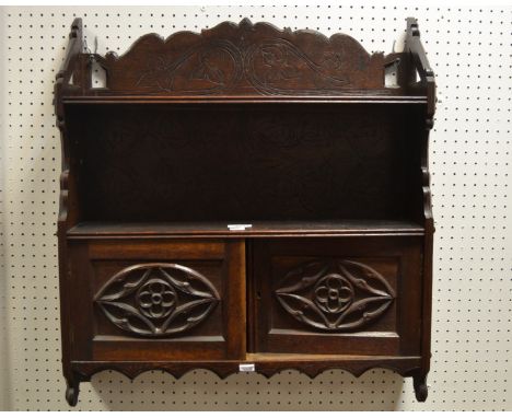 An Arts and Crafts oak wall hanging shelf unit, shaped super structure, carved with vines, pierced shaped supports, two cross