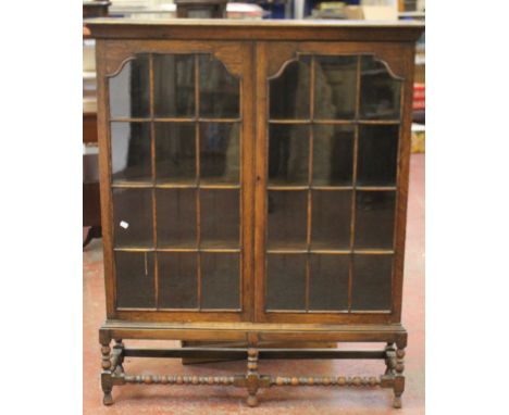 A 1930's oak two door display cabinet with bobbin turned supports, height 137cm