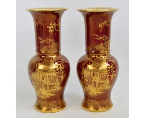 A matched pair of Carlton Ware gilt heightened Rouge Royal vases decorated with pagodas in landscapes, both drilled and conve