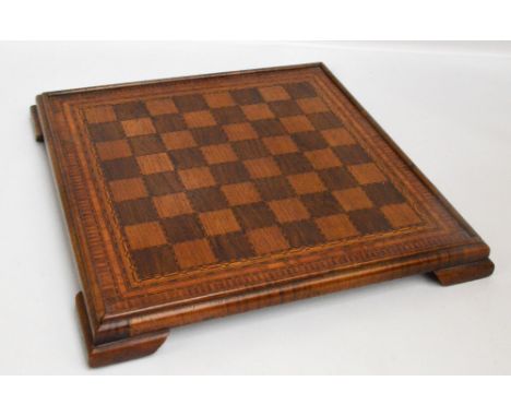 An early 20th century chess board made from specimen woods with stringing and crossbanding, raised on four dumpy bracket feet