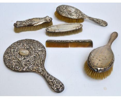 Six variously hallmarked silver backed dressing table items including a circular hand mirror with overall foliate scroll and 