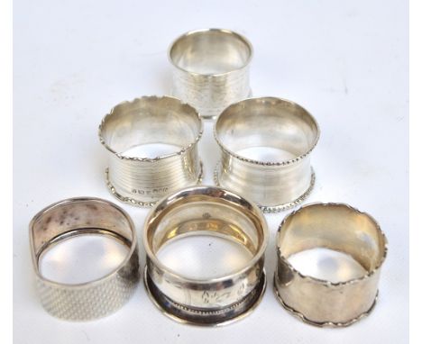 A group of six English variously hallmarked silver napkin rings including a plain circular example with shaped cast rim, init