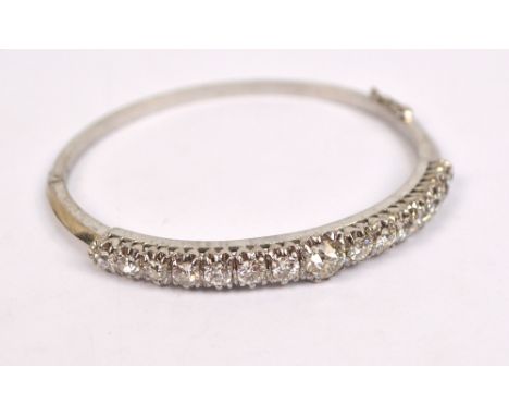 A white metal and diamond set hinged bangle, the principle stone weighing approx 0.75cts, flanked by fourteen slightly gradua