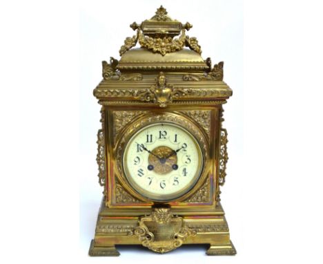 A c.1900 brass mantel clock with swagged finial, scrolling foliate brackets to corners, a gargoyle face above a shield, with 