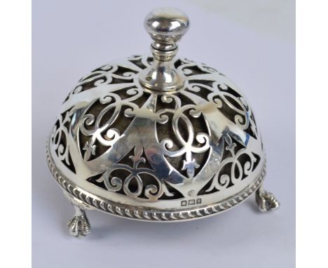 A George V hallmarked silver counter bell with circular domed pierced scroll decorated body, raised on three claw-and-ball fe
