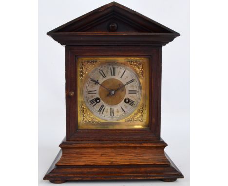 A late 19th century German oak eight day mantel clock with shaped pediment above rectangular brass face with silvered chapter