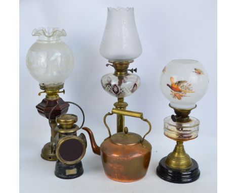 A late Victorian brass oil lamp with clear glass and ruby tinted reservoir, two further oil lamps, a copper and brass kettle,