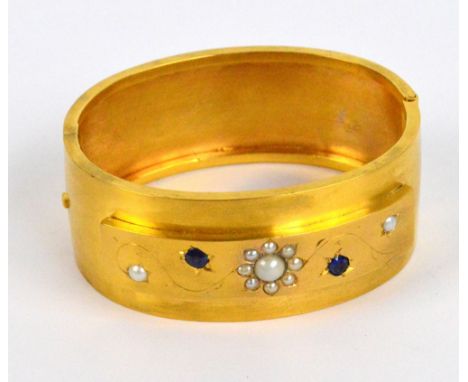 A Victorian yellow metal cultured pearl and sapphire set oval hinged snap bangle, the raised platform set with a floral spray