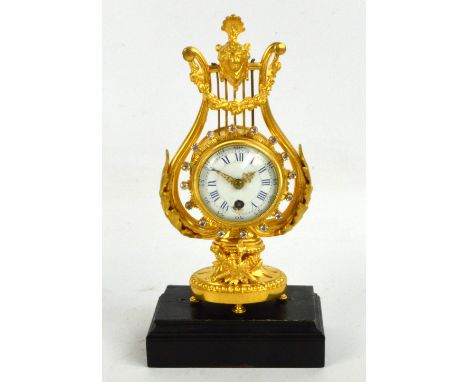 A decorative gilded lyre shaped mantel clock, the white enamel dial set with Roman numerals and raised on an associated plint