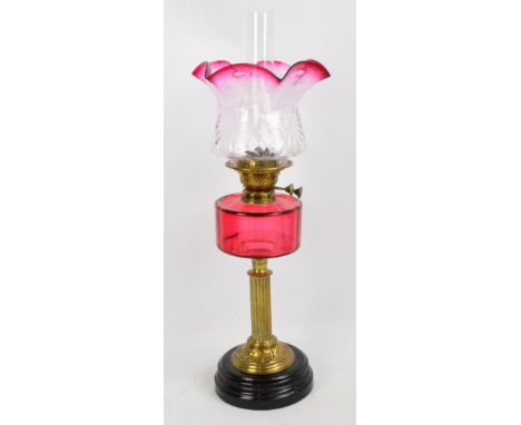 A late Victorian oil lamp with floral moulded clear glass and cranberry tinted shade above cranberry tinted reservoir and flu