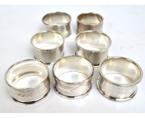 A group of seven English variously hallmarked silver engine turned decorated circular napkin rings with cast decorated border