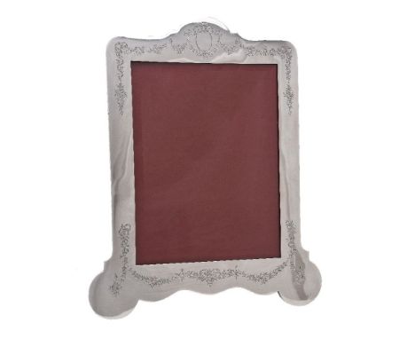 A silver large photograph frame by W. &amp; G. Neal, London 1911, arch centred top and shaped rectangular, engraved with a va