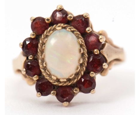 A 9ct opal and garnet ring, the central oval opal cabochon in a rope twist mount, surrounded by small round garnets, with tap