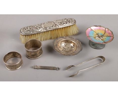 A collection of silver items. Includes enamel dish, pencil, sugar tongs, napkin rings, brush etc.  