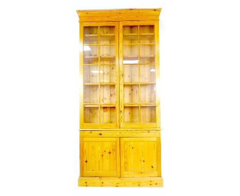 A modern pine bookcase, twin glazed doors, each with ten panes, enclosing four shelves, slide with leather inset, below twin 