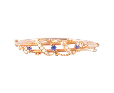 A Victorian yellow gold half hinged bangle, three synthetic blue stones, individually claw set, five seed pearls set in a scr