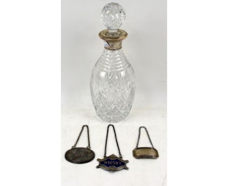 Silver-mounted glass decanter and bottle label, together with an enamelled decanter label for Whisky and a further Gin label 