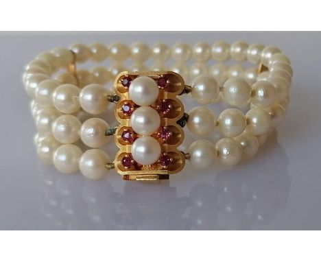 A cultured pearl triple strand bracelet, 18 cm, with a gold and ruby clasp, 23 x 15mm, stamped 750, each pearl approximately 