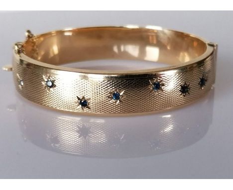 A star-set sapphire and gold bangle with engine turned decoration, 60mm, hallmarked 9ct, 24.3g