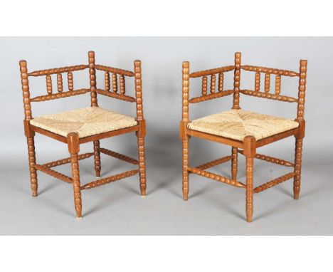 A pair of early 20th century French oak bobbin turned corner chairs with rush seats, height 70cm, width 59cm, depth 58cm.