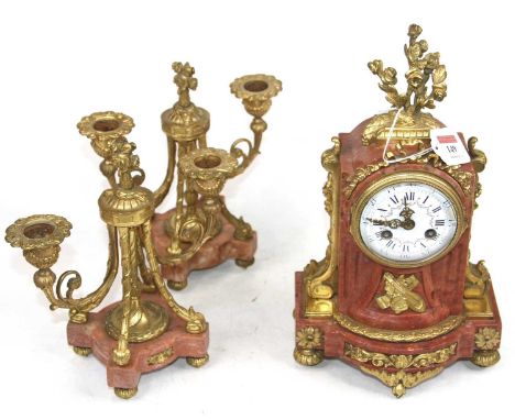 A 19th century French red polished hardstone and gilt metal clock garniture, the enamelled dial showing Roman numerals, havin