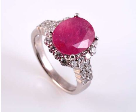 A RUBY AND DIAMOND RING
The oval cut ruby four claw set raised above and within a bezel of sixteen brilliant cut claw set dia